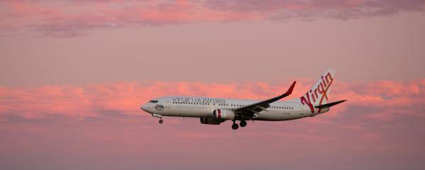 Virgin Australia aircraft arriving with pink skies behind it